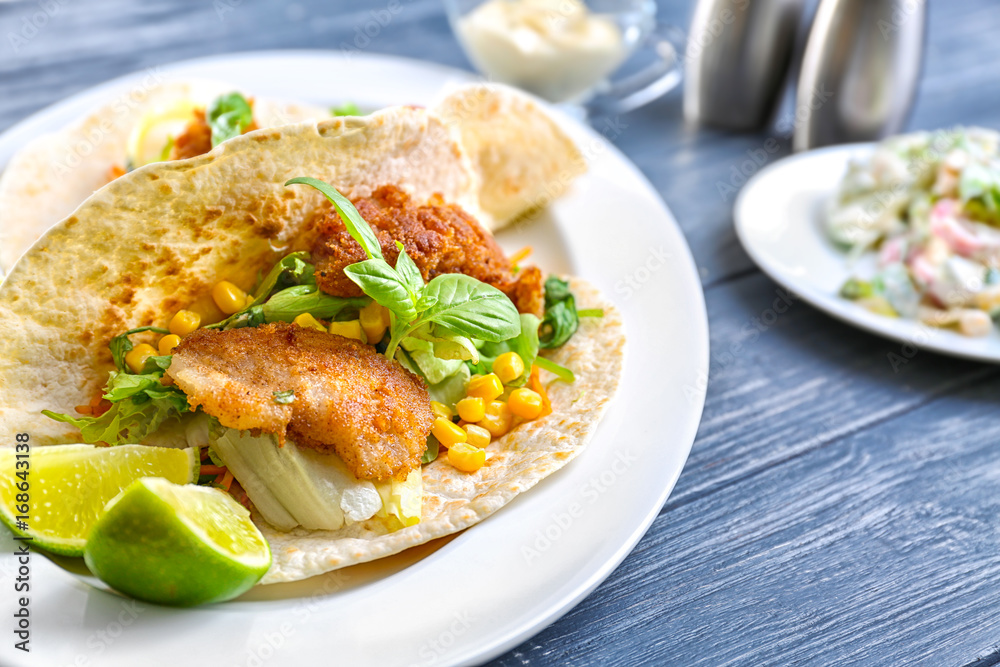 Delicious fish taco on white plate on blue dark table Delicious fish taco on white plate on blue dark table