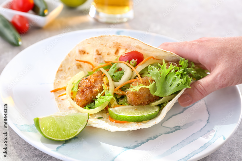 Hand taking delicious fish taco on plate on grey table Hand taking delicious fish taco on plate on grey table