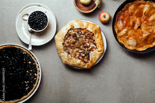 Variety of autumn pies: blueberry tart, chantarelle galette and classical apple pie with sweet pastry crust. Harvest time baking concept. Concrete rustic background. Space for text.