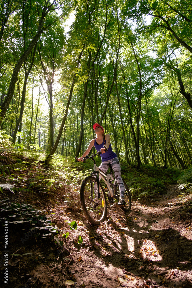 young girl in sport wear with bicycle riding in forest in summer