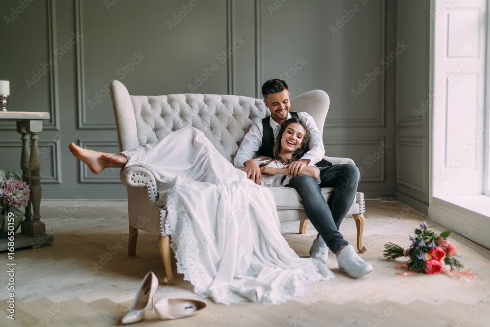 Φωτογραφία Young bride in tender lace dress lies on knees of a handsome groom in blue jeans