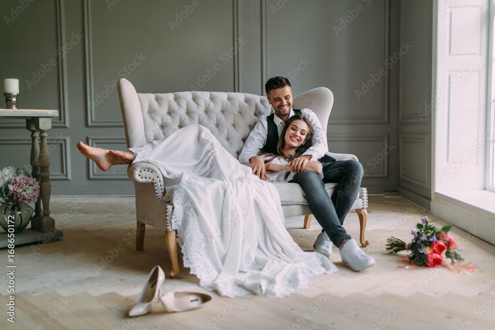 Φωτογραφία Young bride in tender lace dress lies on knees of a handsome groom in blue jeans