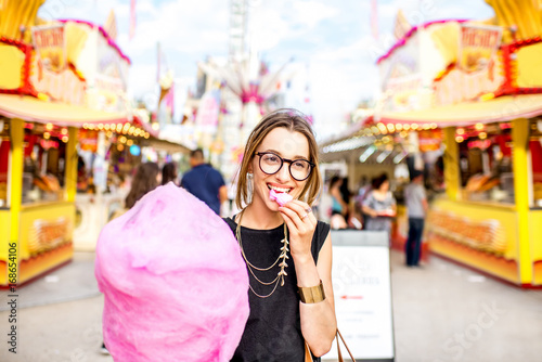 Young woman walking with pink cotton candy outdoors at the amusement park