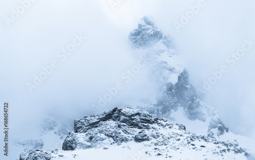 Peak of snowy mountain surrounded by fog and clouds
