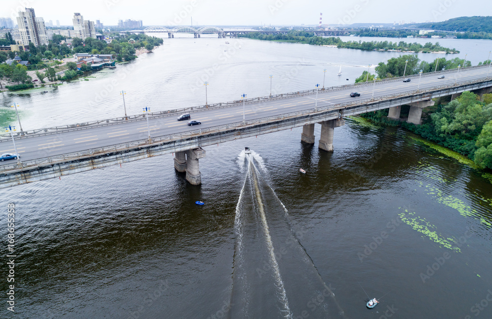 Aerial view of the bridge and the road over the Dnepr River over a green island in the middle of the river with boats. Kiev, Ukraine Aerial view of the bridge and the road over the Dnepr River over a green island in the middle of the river with boats. Kiev, Ukraine