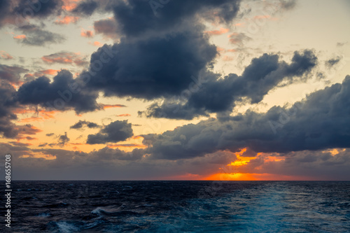Sunset and dramatic set of clouds drifting over the tropical waters of the Caribbean Sea are lit by the last moments of daylight.