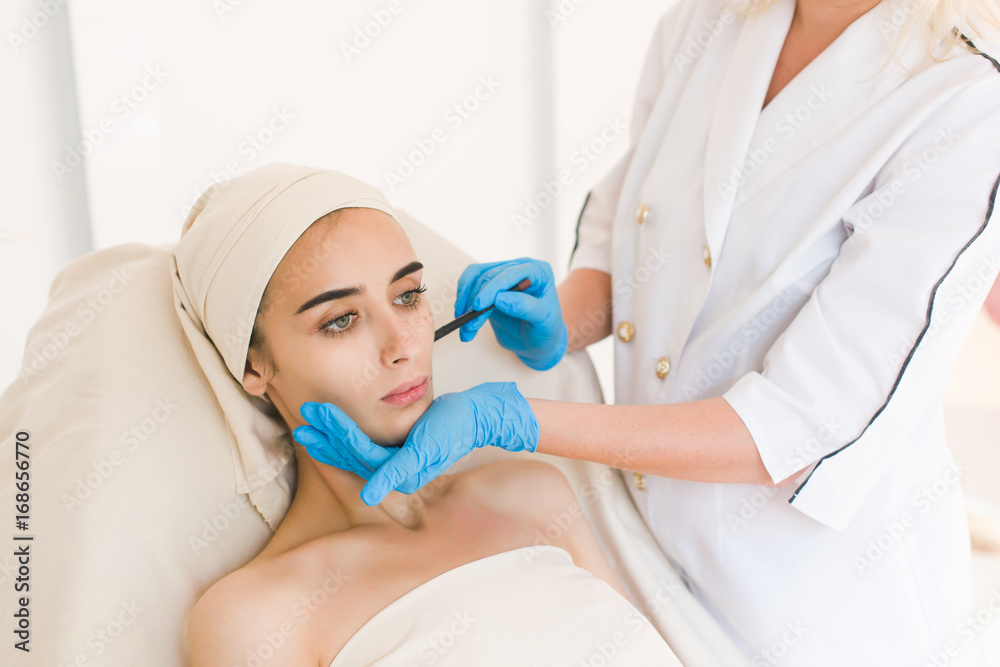 Plastic surgery concept. Doctor drawing marks on female face against white background Plastic surgery concept. Doctor drawing marks on female face against white background