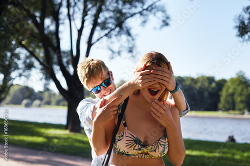 Guess who?! Cheerful playful young male wearing shades covering eyes of beautiful surprised blonde woman in summer cropped top who is trying to guess who is this. People, lifestyle, romance and fun
