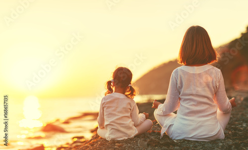 Happy family mother and child doing yoga, meditate in lotus position on beach