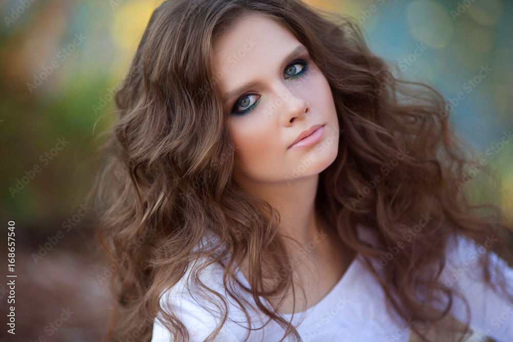 Beautiful young girl of European appearance with makeup and hairstyle, in a white dress, sitting in the autumn forest near the river