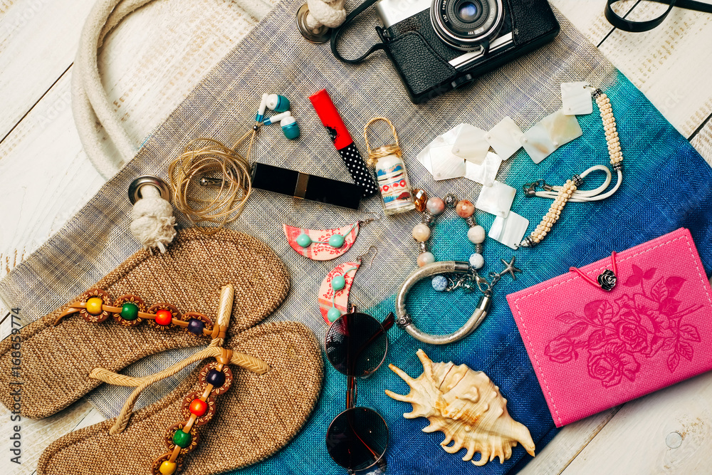 Flat lay of summer fashion with camera, slippers, sunglasses and other girl accessories on top of the bag on white wooden background Flat lay of summer fashion with camera, slippers, sunglasses and other girl accessories on top of the bag on white wooden background