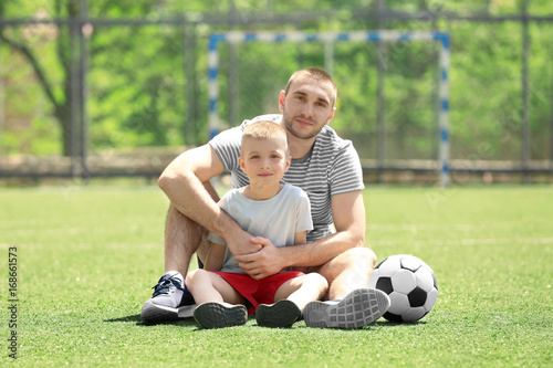 Father and son with ball sitting on soccer pitch