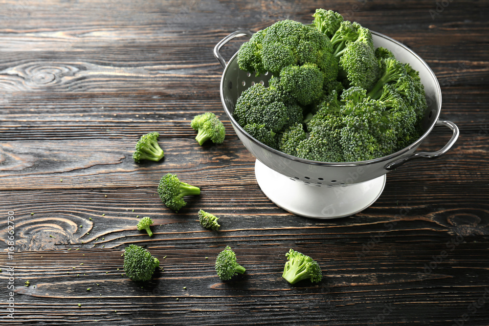 Fresh green broccoli in colander on brown wooden table Fresh green broccoli in colander on brown wooden table