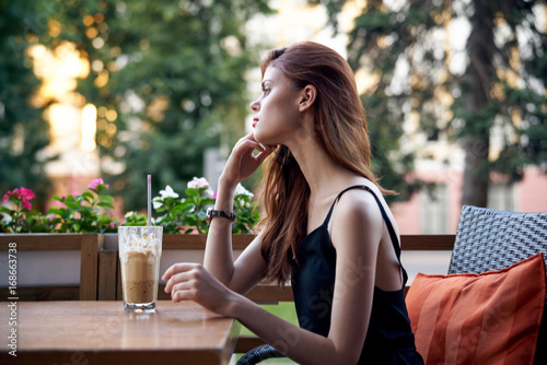 Beautiful woman sitting at a table in a cafe on the terrace in summer, latte, coffee