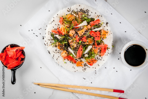 Trend hybrid food. Japanese, Asian cuisine. Sushi pizza with salmon, hayashi wakame, daikon, pickled ginger, red caviar. On a white marble table, with chopsticks and soy sauce. Copy space top view