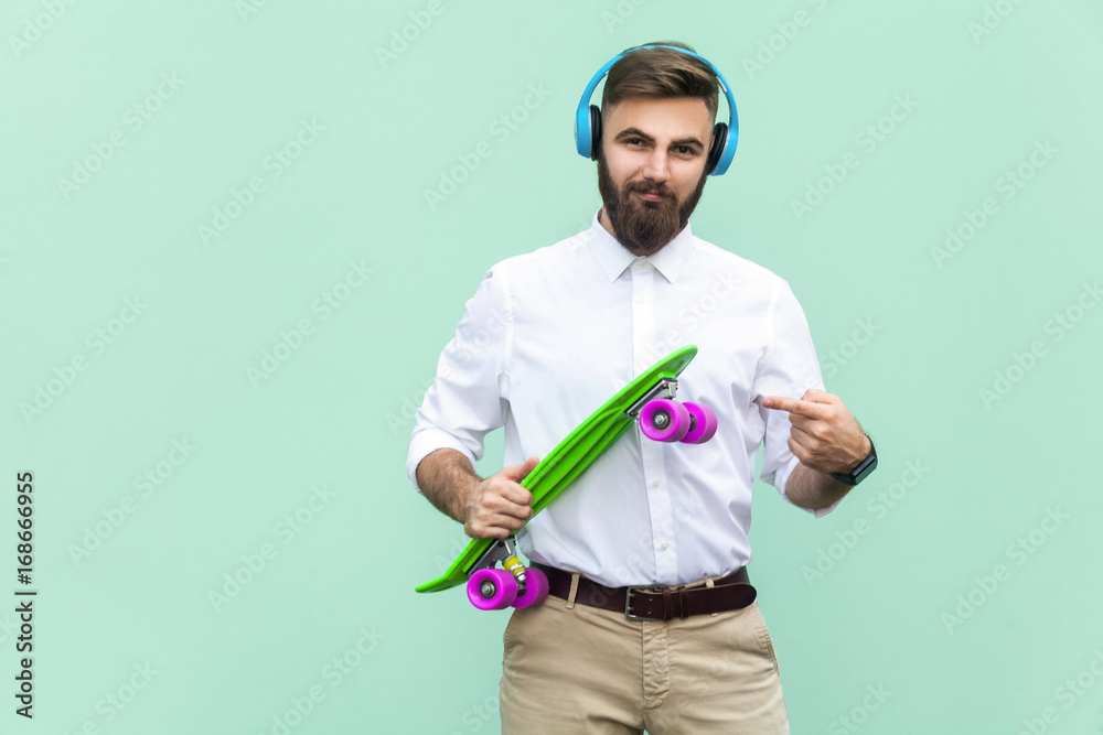 Steep young man with blue headset and holding arms penny skateboard. Light green background. Studio shot Steep young man with blue headset and holding arms penny skateboard. Light green background. Studio shot