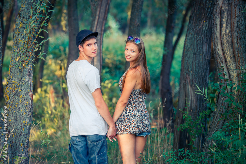 Young loving guy with a girl holding hands. The boy and the girl turned around, entering the forest.