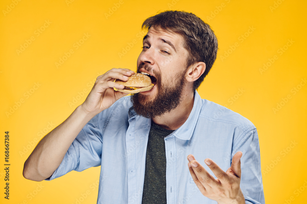 Man on a yellow background eating a hamburger Man on a yellow background eating a hamburger