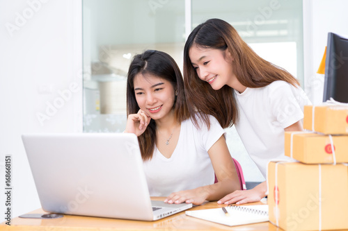 Young asian girl together freelancer business private working at home office with laptop, note, mobile, packaging delivery online market on purchase checking orders to customer. © Kiattisak
