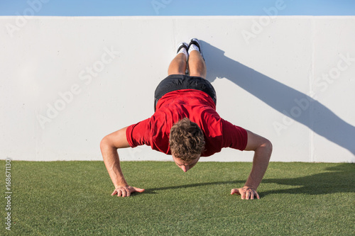 Push up fitness man training using wall doing decline pushup at outdoor gym. Male fitness athlete doing advanced push-ups on grass park.