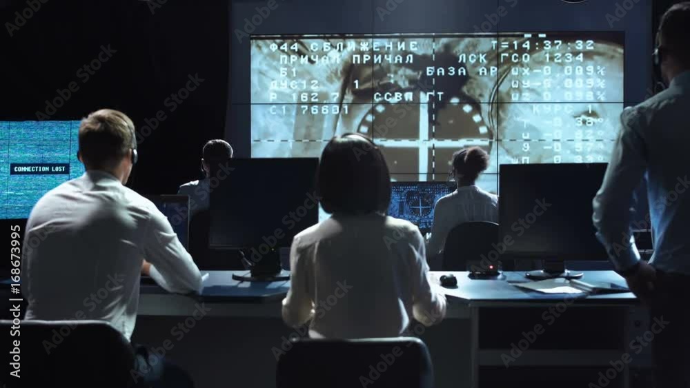 Back view of people working and managing flight in mission control center. Docking to the international space station in space then celebrate. Elements of this image furnished by NASA.