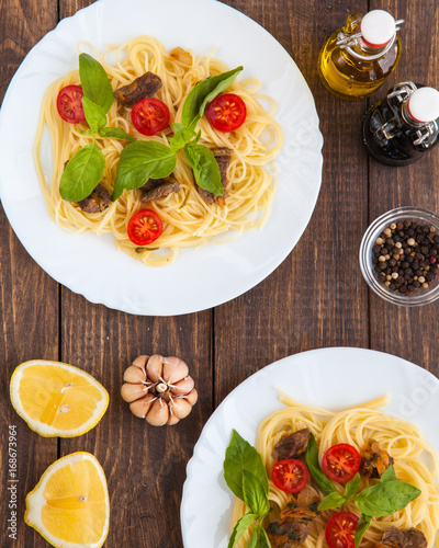 Two dishes of Spaghetti with beef meat slices, cherry tomatoes and basil leaves on white plate. Rustic wooden table  on background. Ideas for restaurant menu. 