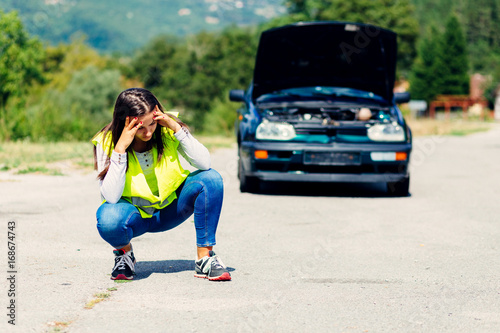 Desperate young female in front of the broken car calling for help 