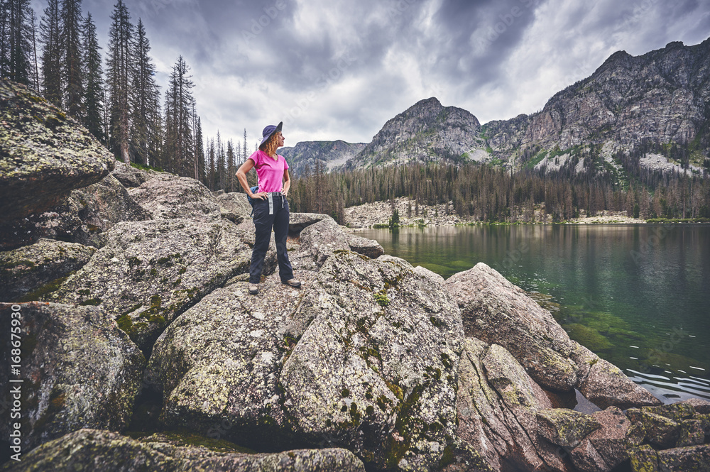 a young woman standing on boulders next to a mountain lake