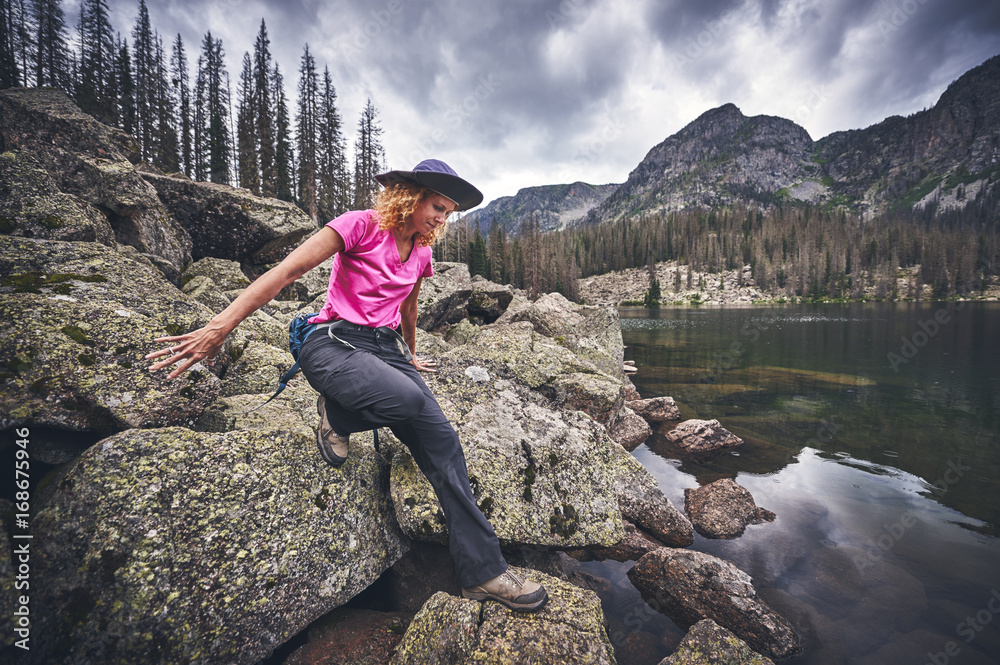 Fototapeta premium a young woman climbing on boulders next to a mountain lake