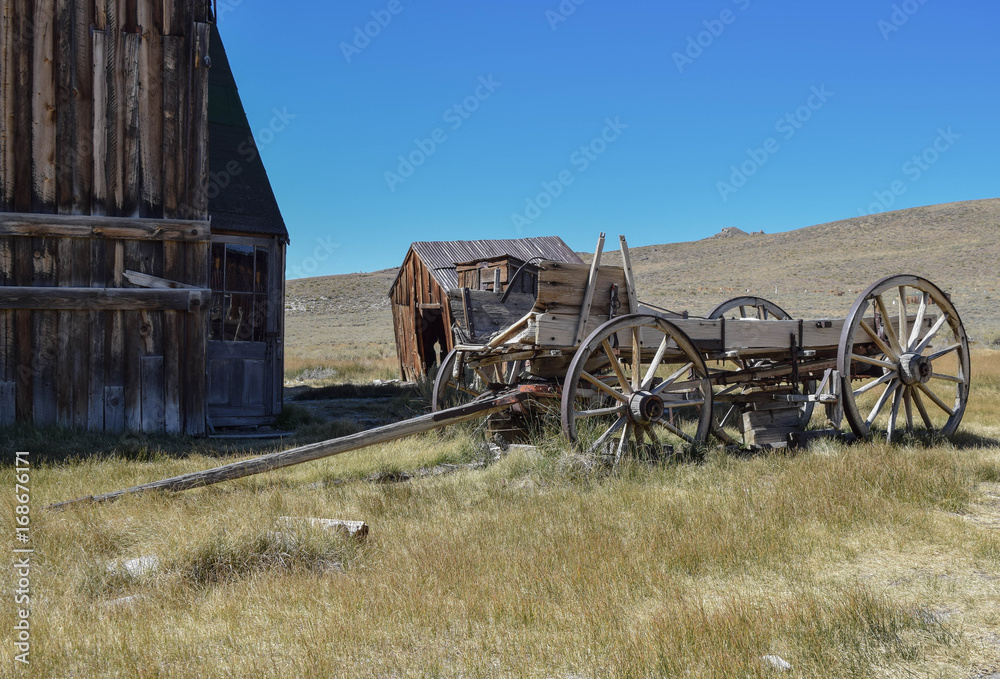 Obraz premium An old barn, outhouse, wagon, deep blue sky, and a beautiful field, in the historic ghost town, Bodie
