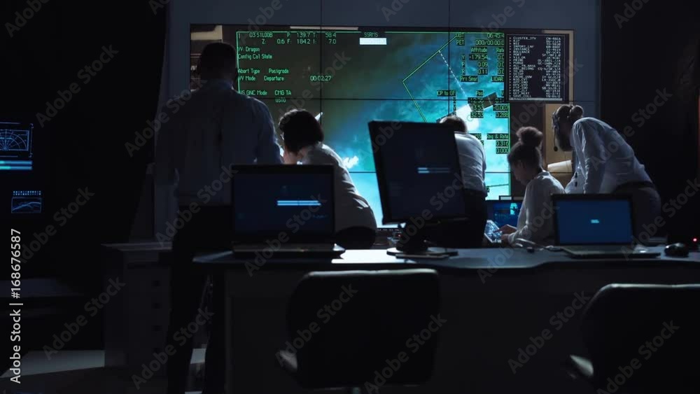Back view of people working and managing flight in mission control center. Elements of this image furnished by NASA.