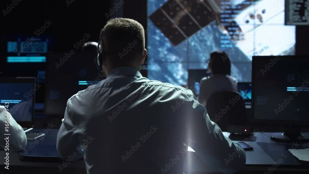 Movement shot back view of man working on space mission in control center. Observing the flight of a satellite in orbit. Elements of this image furnished by NASA.
