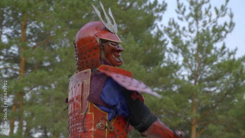 A samurai in red armor and a demon mask runs to the ninja in a black kimono and attacks him with a two-handed katana A samurai in red armor and a demon mask runs to the ninja in a black kimono and attacks him with a two-handed katana