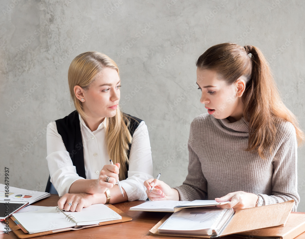 Young caucasian businesswoman discussing with colleague about business plan on table Young caucasian businesswoman discussing with colleague about business plan on table