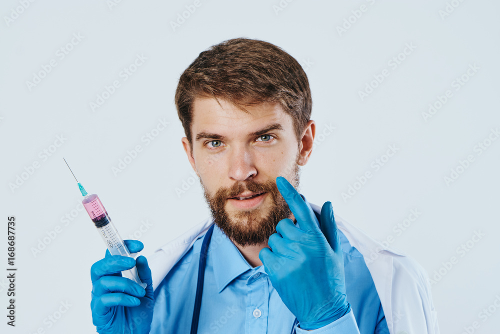Man with a beard on a light background in a medical dressing gown holds a syringe, portrait Man with a beard on a light background in a medical dressing gown holds a syringe, portrait