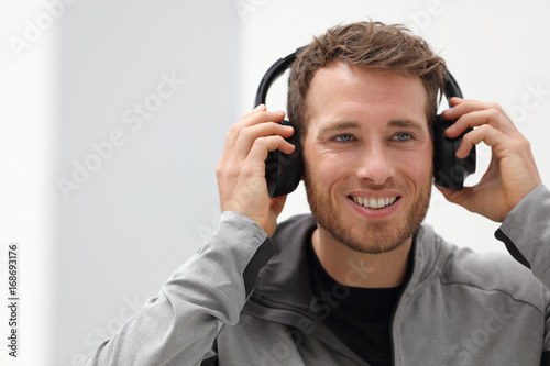 Man putting on headphones to listen to music mobile phone app. Happy smiling young urban person wearing headset sing smartphone mobile app listening to songs in living room at home.