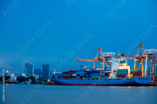 Shipping port. Logistics and transportation of international import export container cargo ship with crane bridge in harbor at twilight dusk for shipping and transportation industry