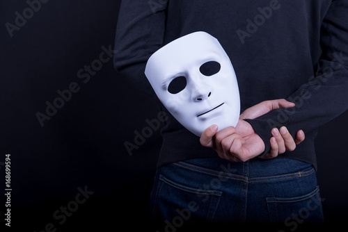 Mystery man holding white mask in the back. Anonymous social masking concept.