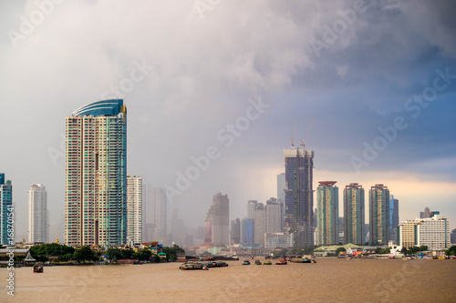 Bangkok skyline cityscape. Buildings, river and boat transportation, ferris wheel at twilight with rain storm and dark cloud and  red sky © Pawin