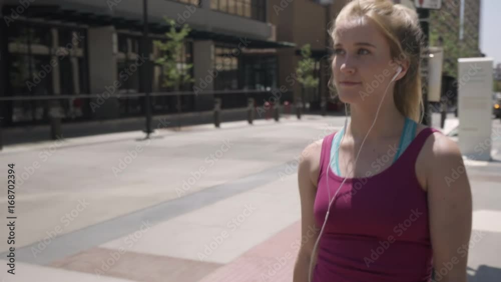 Athletic Young Woman Walks Around Downtown For Exercise, She Listens To Music And Checks Her Smartphone Athletic Young Woman Walks Around Downtown For Exercise, She Listens To Music And Checks Her Smartphone