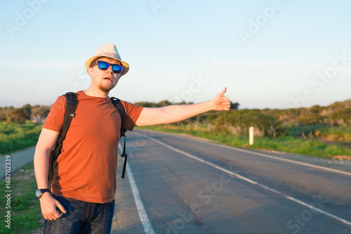 Man with Backpacks in casual Travel Clothes walking along road ,Road hitch-hiking. Traveler standing at the highway hitching © satura_