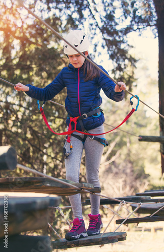 Happy school girl enjoying activity in a climbing adventure park on a summer day