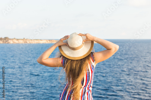 Young woman on the beach near the sea wearing dress and hat, rear view