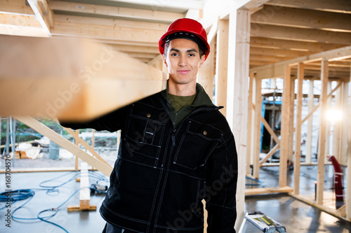 Carpenter Smiling While Carrying Wood At Construction Site