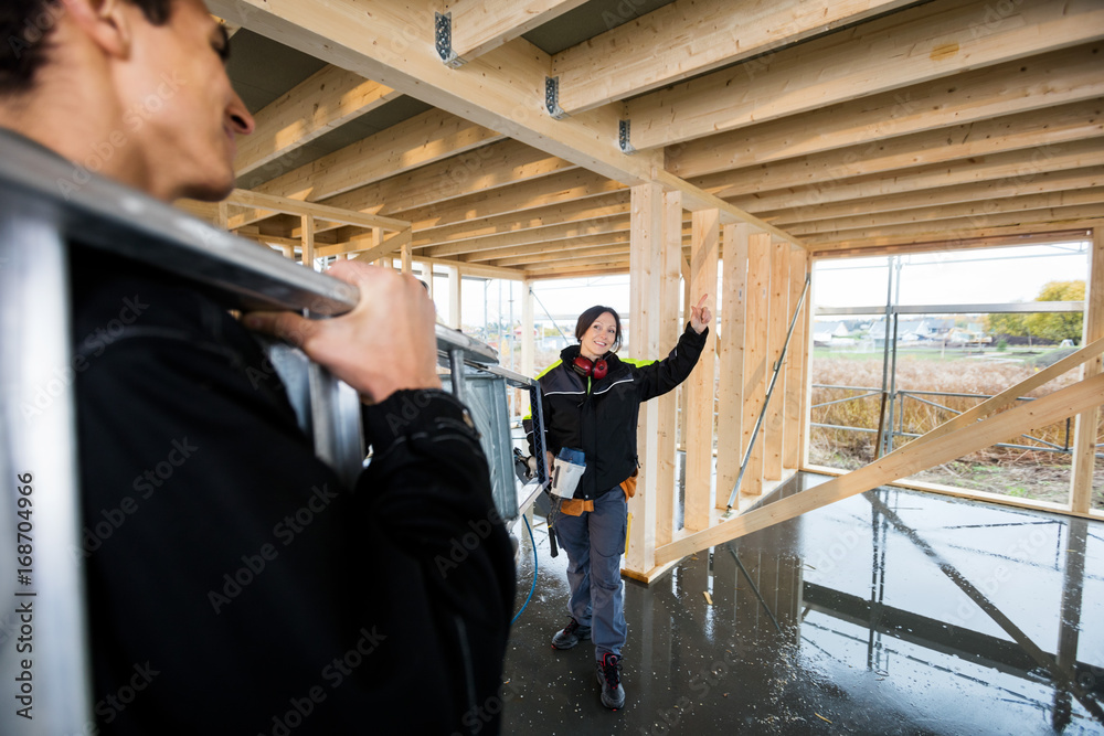Carpenter Gesturing While Colleague Carrying Ladder At Construct Carpenter Gesturing While Colleague Carrying Ladder At Construct