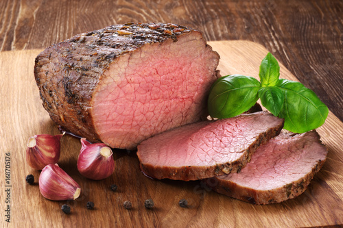 Fotografie Baked meat, garlic and basil on a wooden background. Roast beef.