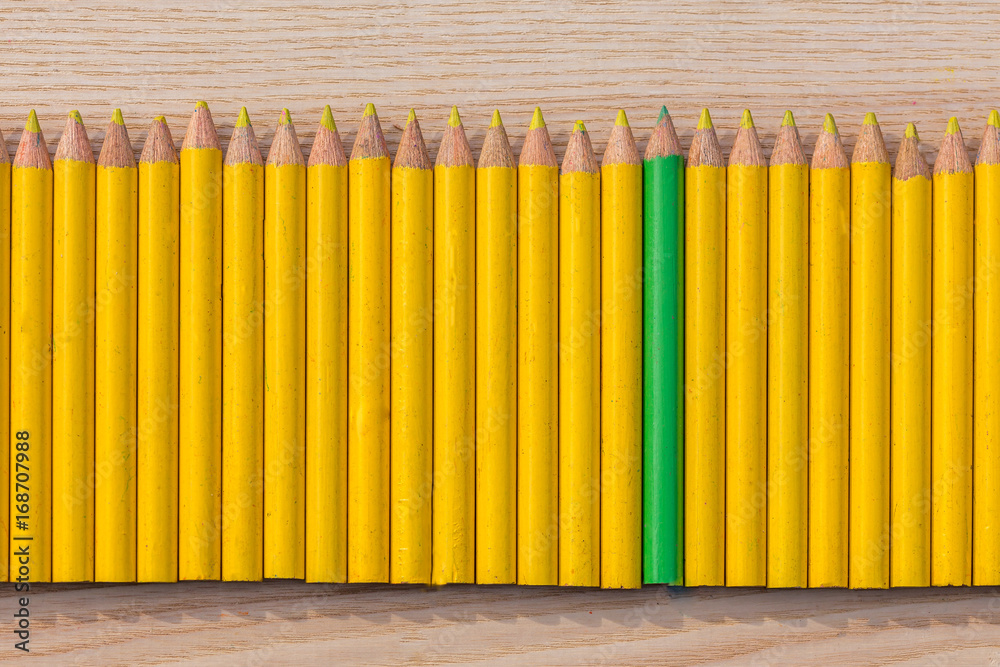 Des petits crayons de couleur jaune alignés avec un crayon vert au milieu Des petits crayons de couleur jaune alignés avec un crayon vert au milieu
