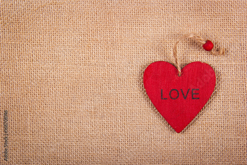 Red wooden heart pendant on a natural linen background. A wooden valentine on a natural background. Backgrounds and textures. Copy space