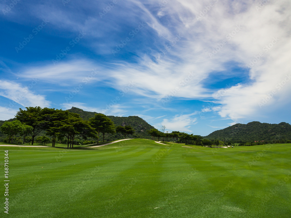 Beautiful golf course fairway with green grass, tropical trees and blue sky in summer