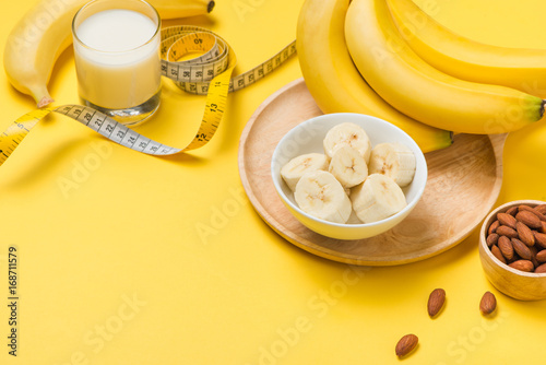 Bananas and almonds with measuring tape on yellow background with copy space